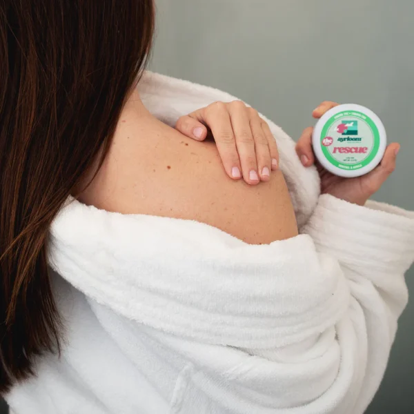 A small container of Ayrloom Rescue Balm with blue and white branding, highlighting menthol and arnica, positioned for easy application.